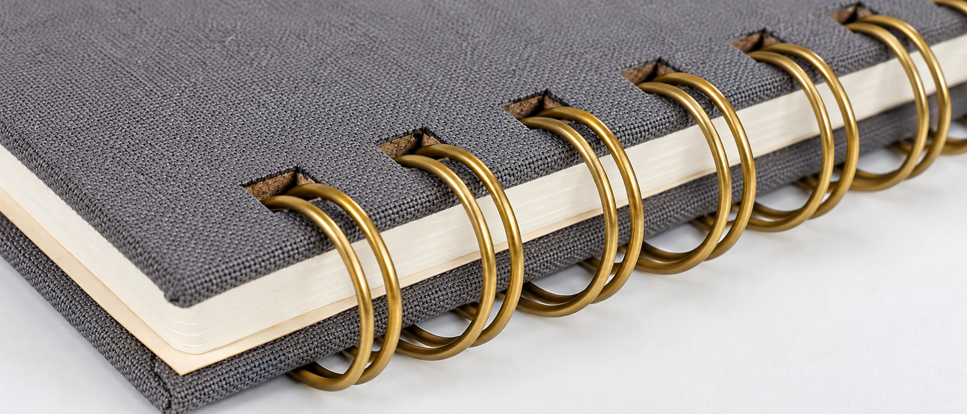 Close-up of gold twin-wire Wire-O binding and rectangular punched holes on a gray cloth hardcover notebook Close-up of gold twin-wire Wire-O binding and rectangular punched holes on a gray cloth hardcover notebook